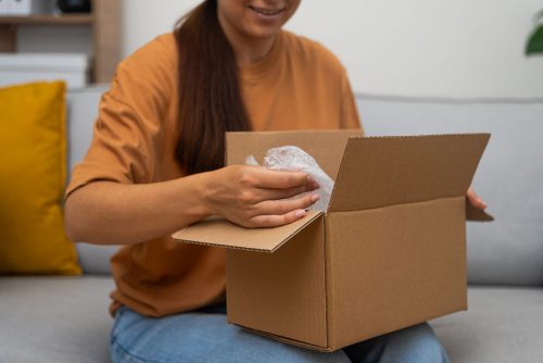 Femme sur son canapé ouvrant un colis Goldcolis, montrant sa joie. Acheter des colis perdus, c’est découvrir des articles inattendus et utiles
