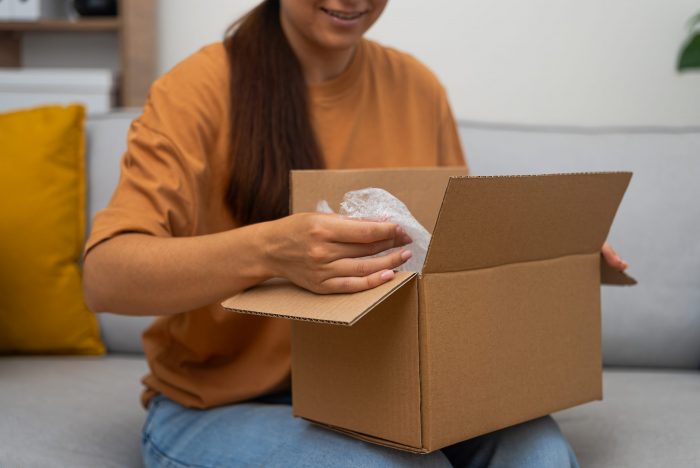 Femme sur son canapé ouvrant un colis Goldcolis, montrant sa joie. Acheter des colis perdus, c’est découvrir des articles inattendus et utiles